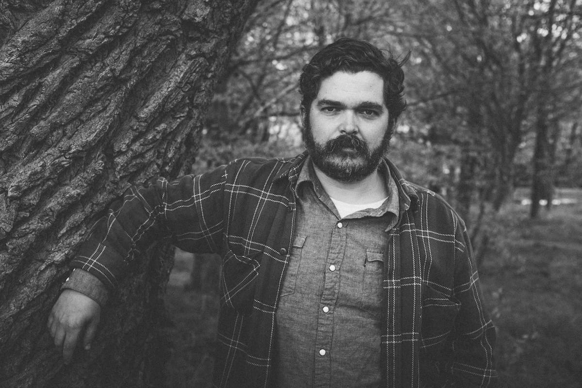 Black and white portrait of cahalen morrison leaning against a tree