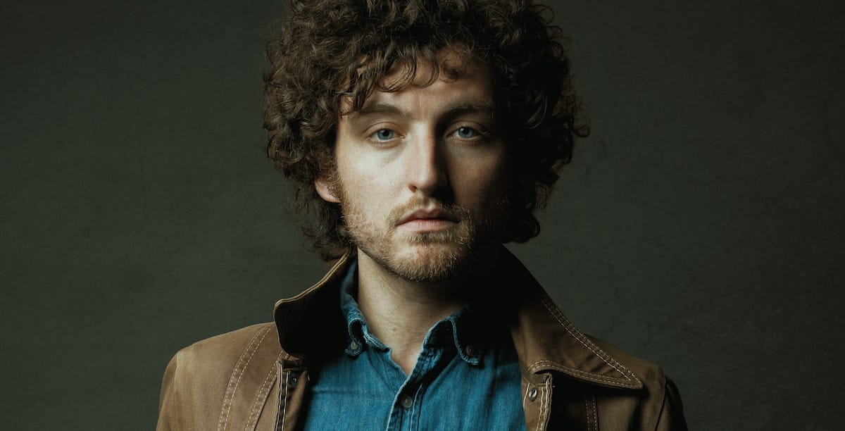 Portrait in color of singer songwriter John Calvin Abney in blue shirt and brown jacket