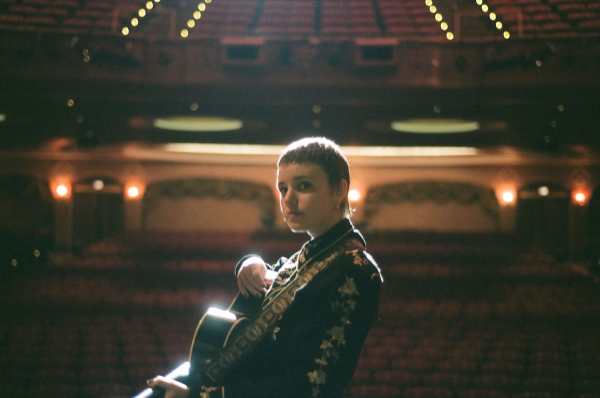 Cat Clyde onstage with acoustic guitar with empty theater seats in the background