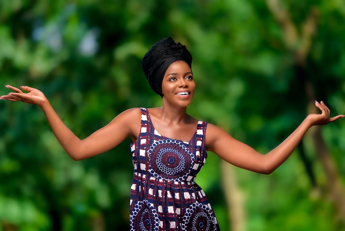 Keturah in African print dress and head wrap against a leafy background
